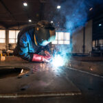 Professional industrial welder welding metal parts in metalworking factory.